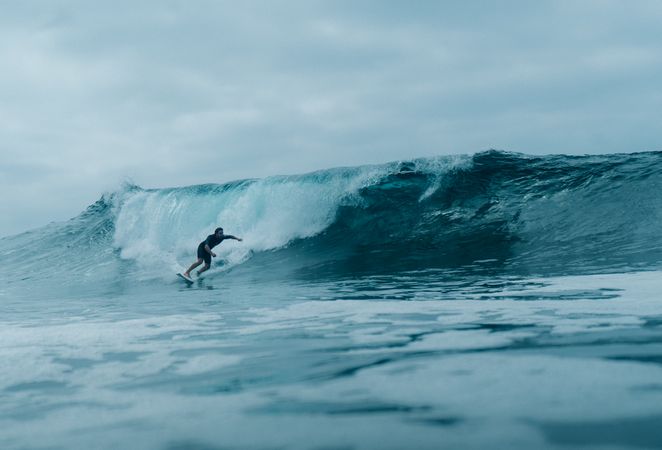 Surfer riding a wave under cloudy sky