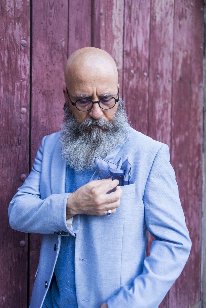 Front view of a mature trendy bearded hipster standing in front o a wood door outdoors