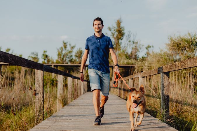 Happy adult man walking with dog along countryside