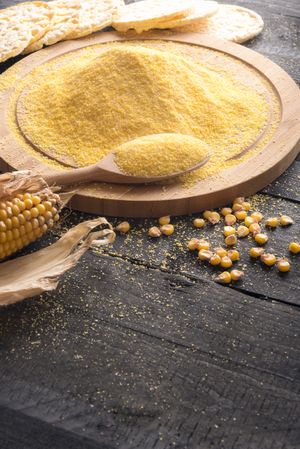 Corn flour on wooden board with kernels and tortillas on wooden table