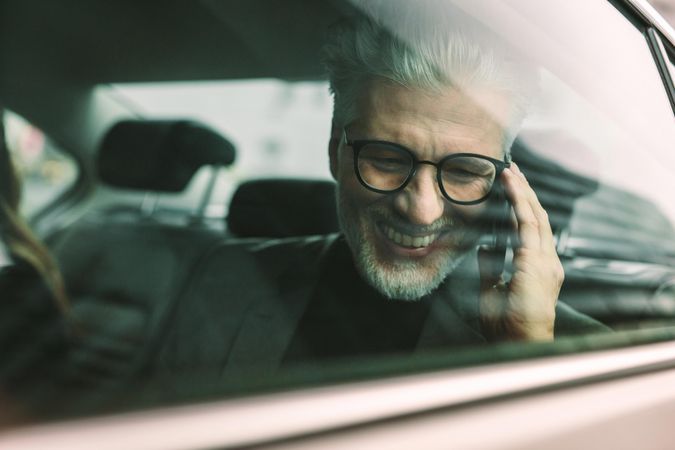 Smiling businessman making phone call while sitting on back seat of a car