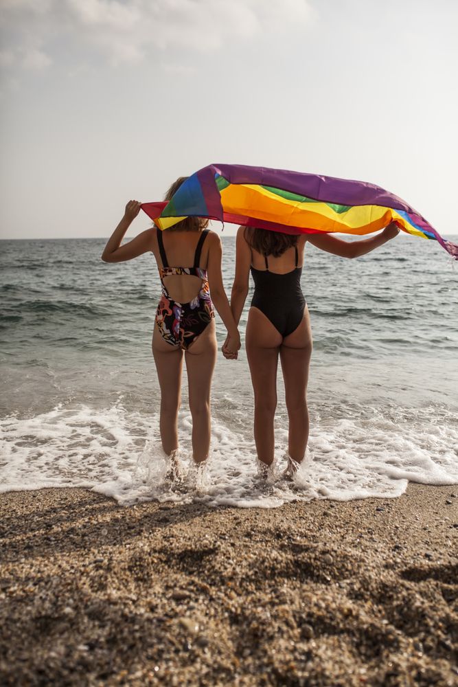 Females standing with rainbow flag on seashore