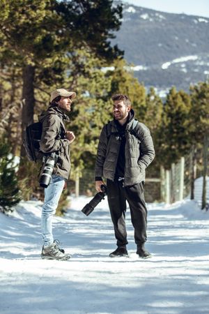 Positive men with cameras talking in winter forest