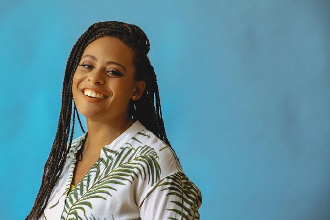 Portrait of confident laughing female with long braided hair in printed leaf shirt, copy space