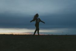 Young woman with long hair spinning in a field at dusk