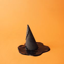 Witch hat made of ice cream cone with melted ice cream on orange background