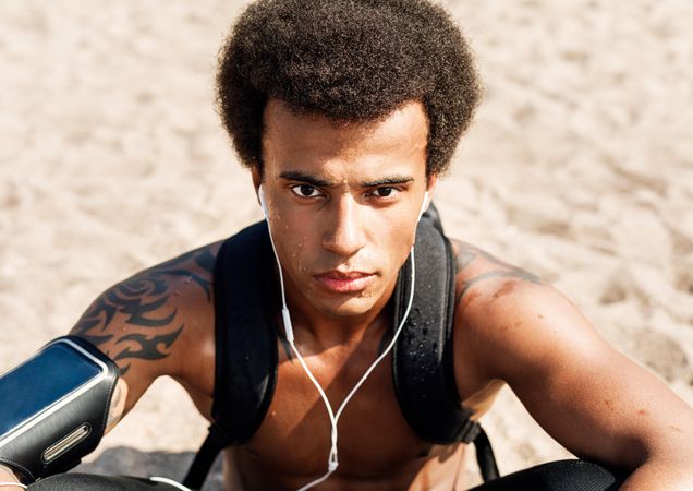 Intense athletic man sitting in the sand with backpack