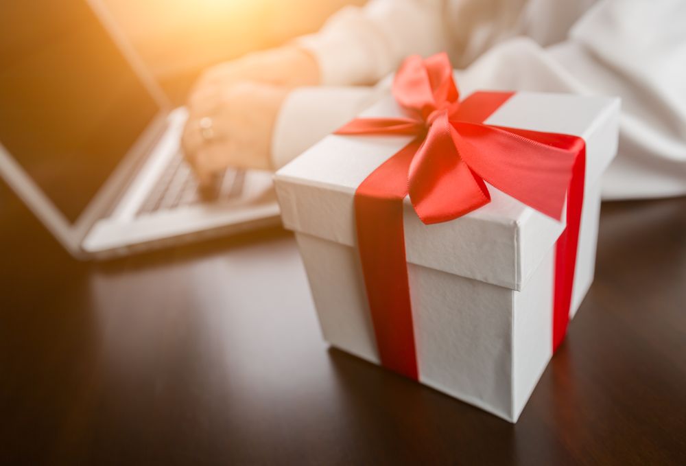 Gift Box with Red Ribbon and Bow Near Man Typing on Laptop Computer.
