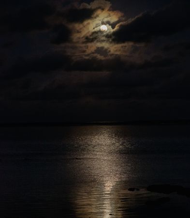 Full moon behind clouds above an ocean