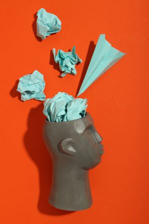 Side of grey bust of head on red background with paper airplane, vertical