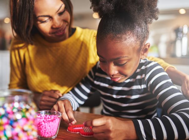 Black mother and daughter creating heart shape craft at home