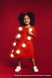 Beautiful girl in red dress holding string of lights around her neck 5Q1Ee5