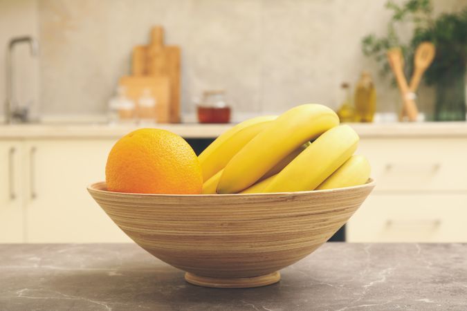 Bowl with fruits on gray table against kitchen interior