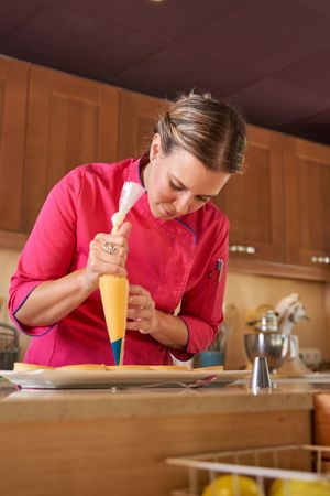 Female pastry chef making peaks of cream on tarts