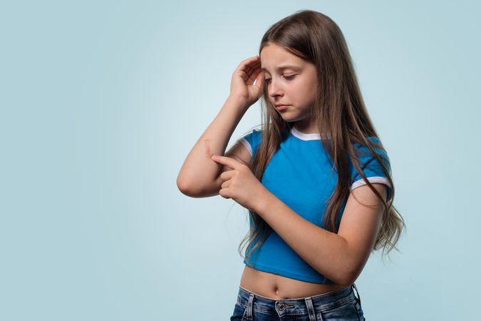 Young girl examining cut on elbow, appearing concerned