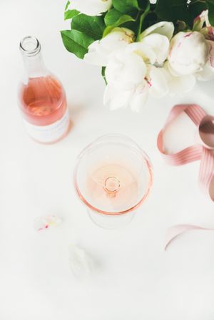 Glass of pink rose wine, and bottle with flowers and ribbon