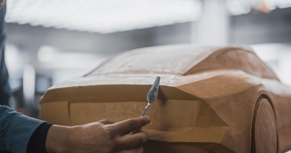 Young Black Man Using a Spatula to Carefully Trim Surface of a Prototype Concept Eco Vehicle
