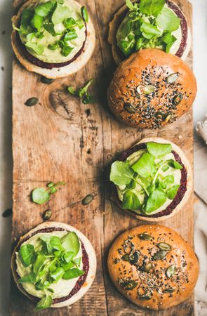 Fresh vegan burgers on seeded buns arranged on wooden board, vertical composition with copy space