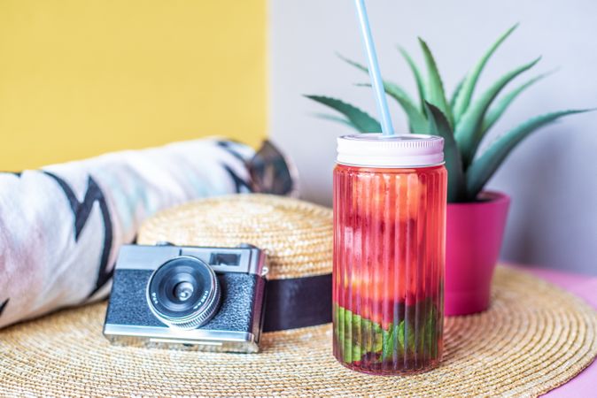 Jar of pink ice tea with straw hat, towel and a camera