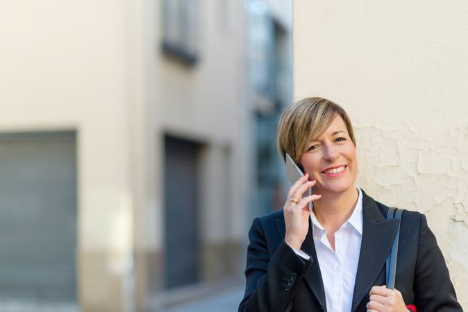 Smiling woman wearing a blazer and speaking on phone outside