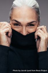 Mature woman playfully covering mouth with dark sweater beooK5