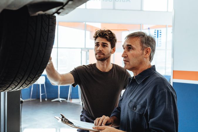 Mechanic showing the wheel of car to colleague making notes in clipboard