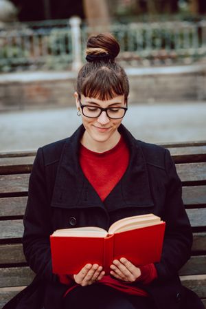 Young woman reading book on bench in park