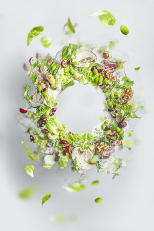 Circle frame of flying healthy green salad with lettuce, nuts, beans, dressing and vegetables. Balanced vegan food with copy space. Levitation of food