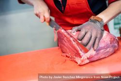 Close up of butcher in apron cutting raw meat bxyRX0