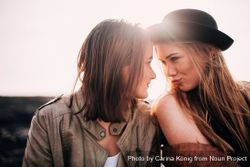 Two young women leaning into each other face to face playfully outside R0JGr5