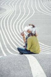 Modern relaxed woman vaping while sitting on marked road