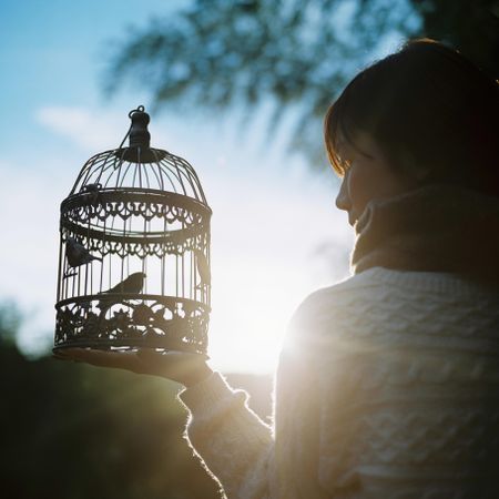 Young person holding a cage with a bird inside outdoor