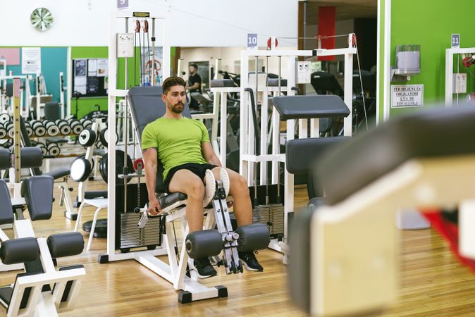 Male in green t-shirt working out legs using gym equipment