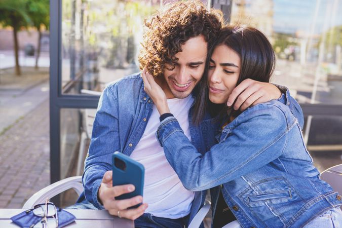 Man and woman embracing while taking selfie sitting down outside