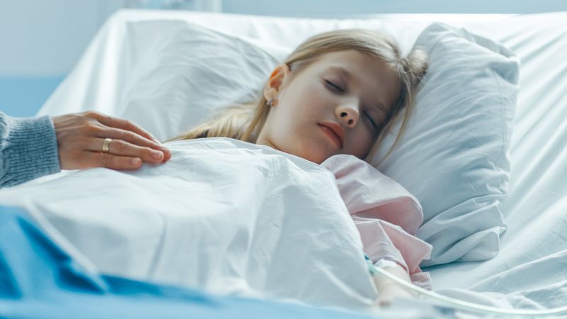 Cute Little Girl Sleeps on a Bed in the Children's Hospital, Caring Mother Covers Her with a Blanket and Caresses Her Forehead