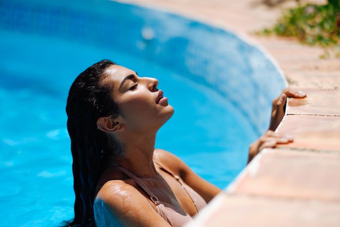Side view Arab woman grasping side of swimming pool with eyes closed