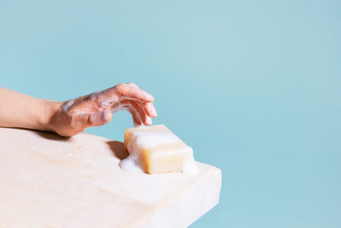 Woman’s hand reaching for bar of soap with foam
