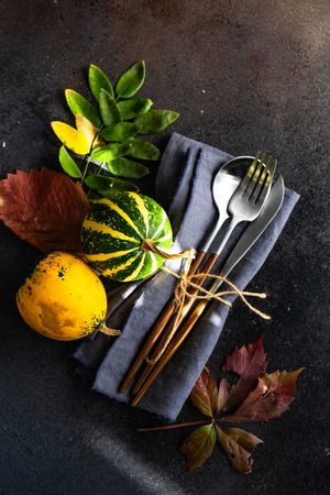 Top view of cutlery on navy napkin with autumn leaves and mini squash