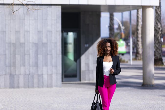 Female in bright pink trousers strolling outside of building
