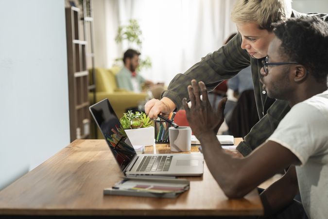 Black and female coworkers pointing at laptop screen together during collaborative home office work session