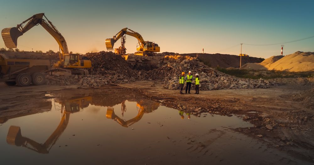 Aerial Drone Shot Of Construction Site With Heavy Machinery On Sunny Day: Diverse Team of Real Estate Developers Discussing Project. Civil Engineer, Architect, Urban Planner Talking, Using Tablet.