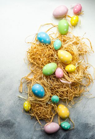 Easter festive card concept with pastel eggs decorations scattered on straw
