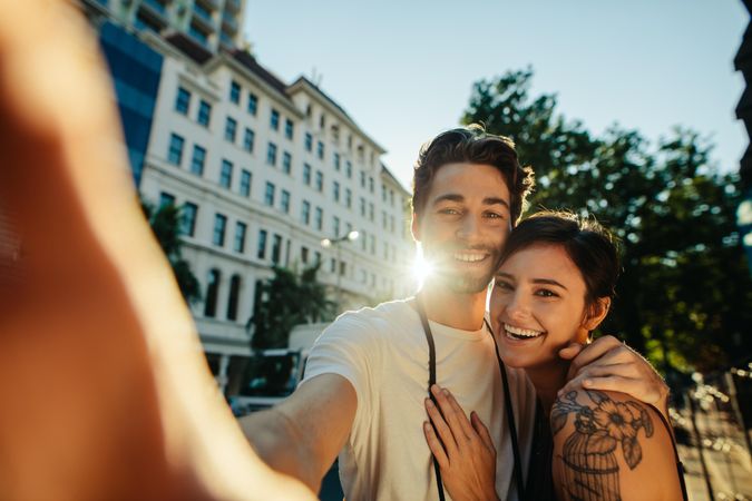 Happy explorer couple taking a selfie standing in the street with sun in the background