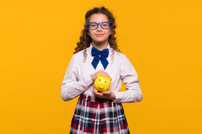 Girl with blue glasses holding yellow piggy bank