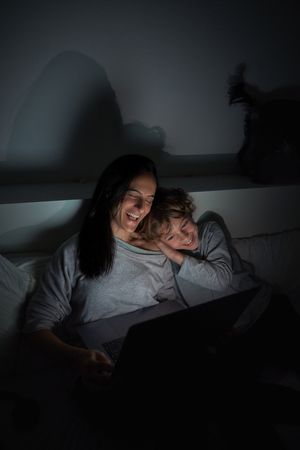 Happy woman with son browsing laptop in darkness