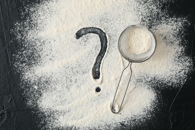 Flour, sieve and question mark on dark background