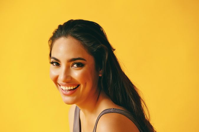 Headshot of Hispanic woman smiling and leaning forward on yellow background