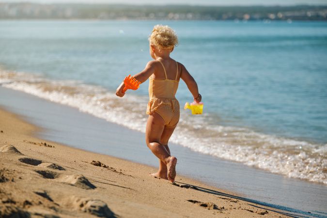 Active girl in swimwear walking next to sea with toys