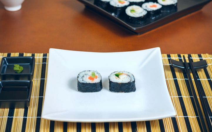 Two freshly made sushi rolls on rectangular plate on mat, ready to eat
