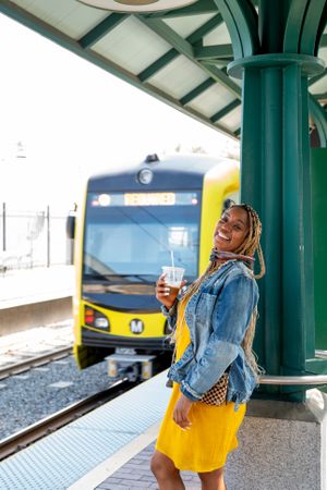 Woman standing on train platform smiling and looking at camera with train in background